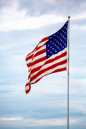 American flag waving on a flagpole infront of clouds