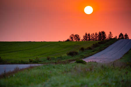 Asphalt road going through Wisconsin farmland in-front of a colorful sunrise, horizontalの写真素材
