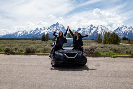 Jackson Hole, Wyoming, USA, May, 28, 2021: Two girls on the hood of a car smiling in front of the...