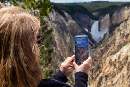 Tourist taking a pic of the lower falls in Yellowstone National Park with her smartphone, horizontalの写真素材