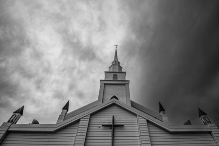 Church steeple with a cross on top rises against a dramatic, cloudy sky, horizontalの写真素材