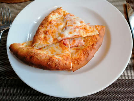 On the table is a white plate, close-up, slices of pizza, next to cutlery, fork and knife.の写真素材