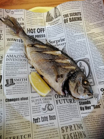 Fried dorado fish with lemon on a newspaper in a restaurantの写真素材