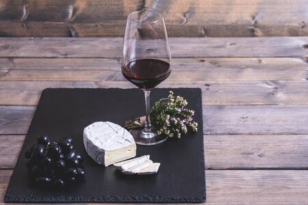 glass of wine, french cheese and grapes on a wooden table.の写真素材