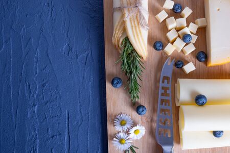 rosemary, daisy, berries and cheese lie on a wooden board on a blue backgroundの写真素材