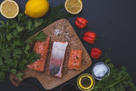 salted slices of salmon, greens and salt lie on a table on a black stoneの写真素材