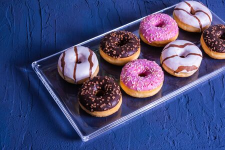 mouth-watering and sweet donuts lie on a glass tray on a blue tableの写真素材