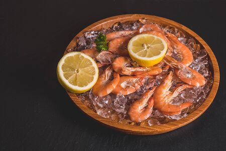 sliced slices of lemon and shrimp lie on ice in a wooden tray on a black backgroundの写真素材