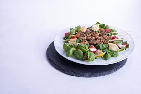a plate of shrimp on sticks and vegetables stands on a black tray on the table on a white backgroundの写真素材