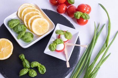basil, mozzarella in red tomatoes and lemon on a white tableの写真素材