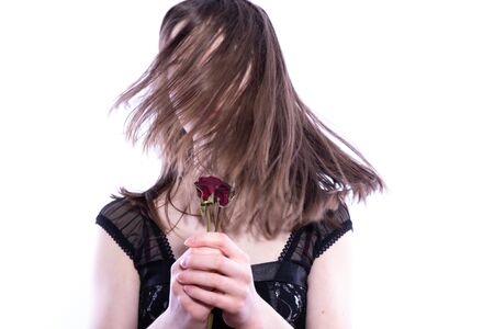 young girl hiding behind her hair and holding three roses in her hands on a white backgroundの写真素材