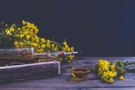 bottle of rapeseed oil near rapeseed flowers on a wooden table on a blue backgroundの写真素材