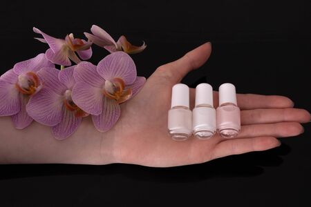 on a female palm lies nail polish and an orchid on a black background