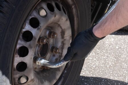 male hands unscrew the bolts on the wheel from the car on the streetの写真素材