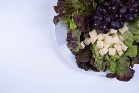salad, slices of cheese and grapes on a plate on a table on a white backgroundの写真素材