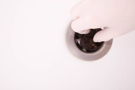 hand cleans a sink in the bathroom, which clogged female hair on a white background