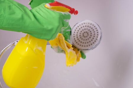a cleaning lady in gloves cleans the bathroom and washes a shower head with detergent on a white backgroundの写真素材