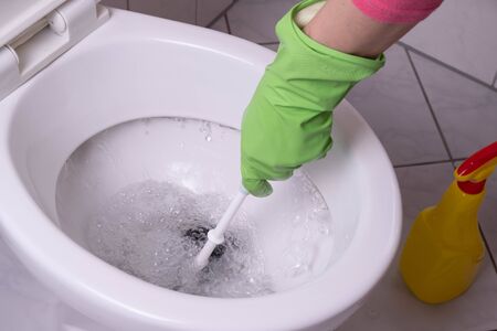 cleaning lady in the bathroom cleans a clogged toilet in green gloves on a white backgroundの写真素材