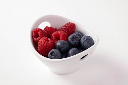 blueberries and raspberries in a cup on a white backgroundの写真素材