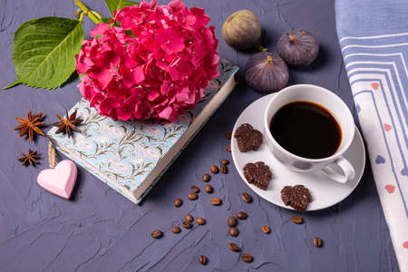 aromaton coffee, book and pink hydrangea pieces of dark chocolate on a saucer and three figs lie on...