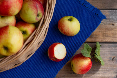 3 apples, one already ask, lie on a blue tablecloth and next to a full basket of apples