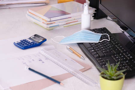 school items and a mask with antiseptic are on the desk, for online home educationの写真素材