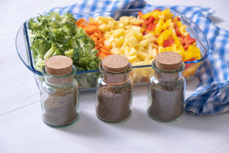 spices for a vegetarian vegetable dish, chopped vegetables in the background in a glass dish
