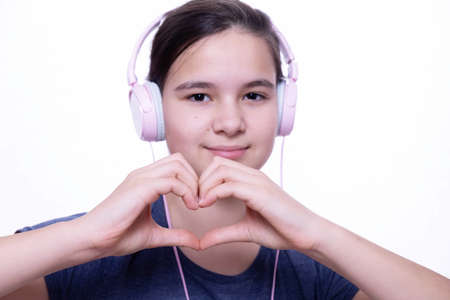 teen girl with headphones on her head, shows a heart symbol, showing love for music