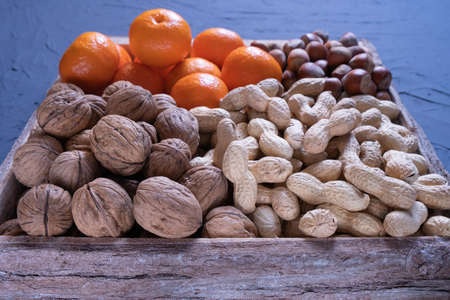 hazelnut, walnut, peanut and tangerines lie in a wooden box against a blue textured background
