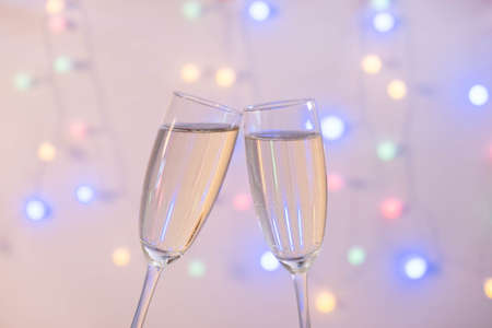 two full glasses of champagne pressed against each other from the back of a garland on a white...