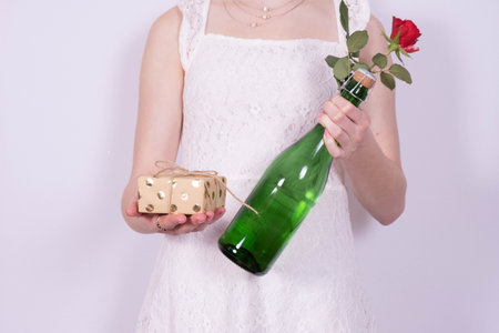 a girl in a dress holds a bottle of champagne in her hand, and in the other a gift on a white backgroundの写真素材