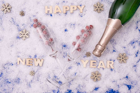 a bottle of champagne and glasses for it lie on the festive table next to the inscription: "Happy New Year" on a snowy backgroundの写真素材