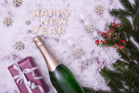 Spruce branches, a gift, sweets, a bottle of champagne and wine glasses lie on the festive table next to the inscription: "Happy New Year" on a snowy backgroundの写真素材