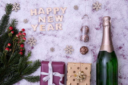 New Year's gifts, fir-tree branches, a bottle of champagne, red berries lie on the festive table next to the inscription: "Happy New Year" on a snowy backgroundの写真素材