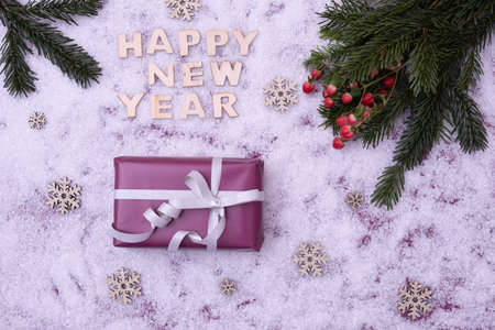 New Year's gift, spruce branches, berries lie on the festive table next to the inscription: "Happy New Year" on a snowy backgroundの写真素材