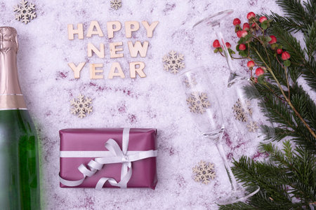 red berries, spruce branches, a gift, sweets, champagne and wine glasses lie on the festive table next to the inscription: "Happy New Year" on a snowy backgroundの写真素材