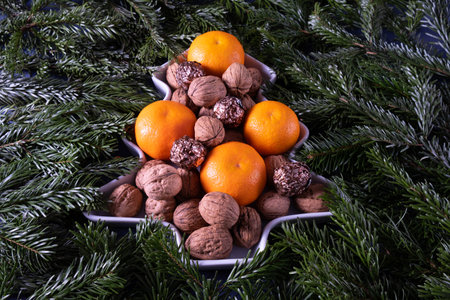 juicy tangerines and nuts on a table in the shape of a Christmas tree on spruce branches, on a blue backgroundの写真素材