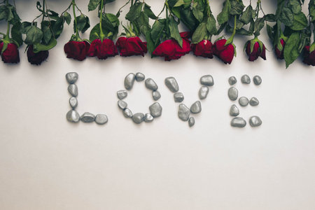 on a white background is the word "Love" laid out of stones, on top of dead roses, top viewの写真素材
