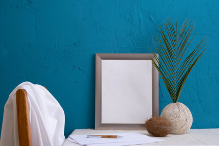 coconut, fern in an old vase, set for writing, gray photo frame on a blue background on the tableの写真素材