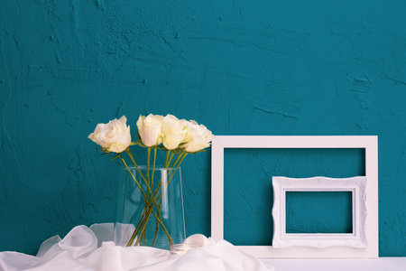 white roses in vase, frame for a picture on a blue background on the tableの写真素材