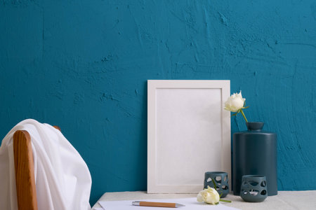 two candlesticks, a set for writing, roses in blue vases, the back of a chair on a blue background on the tableの写真素材