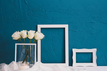 bouquet of white roses in a vase, picture frame on a blue background on the tableの写真素材