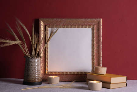 candles are burning, old books, vases with ears of corn, old photo frame on a red background on the tableの写真素材