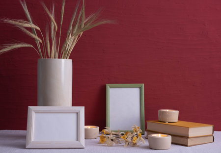 old books, candles are burning, a gray vase with ears of corn, dry daffodils, photo frames on a red...