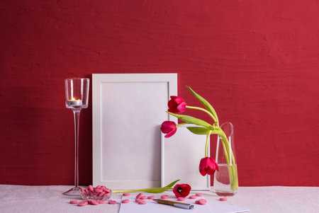 writing materials, tulips in a vase, iron heart, photo frames on a red background on the tableの写真素材