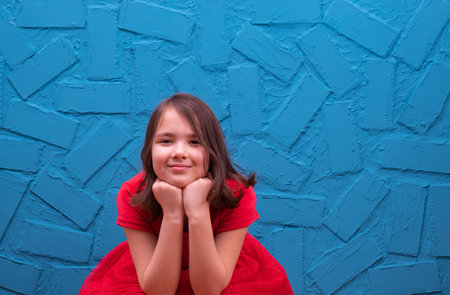 girl in a red dress sits on the floor and dreams, on a blue backgroundの写真素材