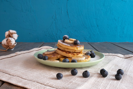 blueberries are scattered on the table and pancakes with honey are in a plate, on the table