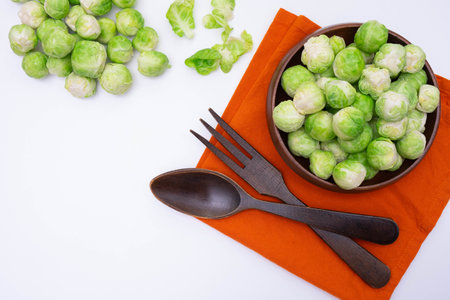 wooden fork and spoon lie on the table, next to Brussels sprouts lies in a wooden bowl on a tablecloth, on a white backgroundの写真素材