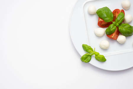 mozzarella, green basil and chopped tomatoes on a white plate on a table and white plateの写真素材