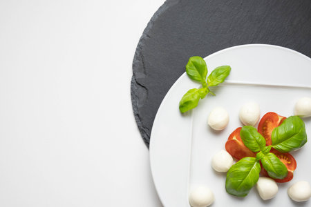 mozzarella, fresh basil and chopped tomatoes on a white plate and on a stone stand on a table and white plateの写真素材